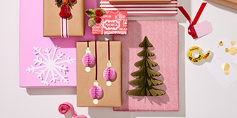 Decoraciones navideñas y manualidades de papel como árboles y bolas adheridas a regalos envueltos usando Cinta de Doble Cara Scotch®
