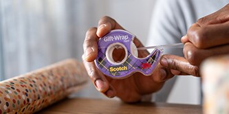 Hombre envolviendo un regalo con cinta Scotch® para envolver regalos
