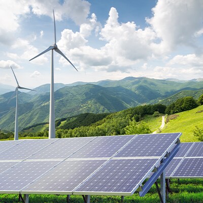 Paisaje montañoso con molinos de viento y paneles solares en primer plano.