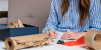 Mujer empaqueta cuidadosamente un regalo y utiliza el protector Scotch™ Cushion Lock™
