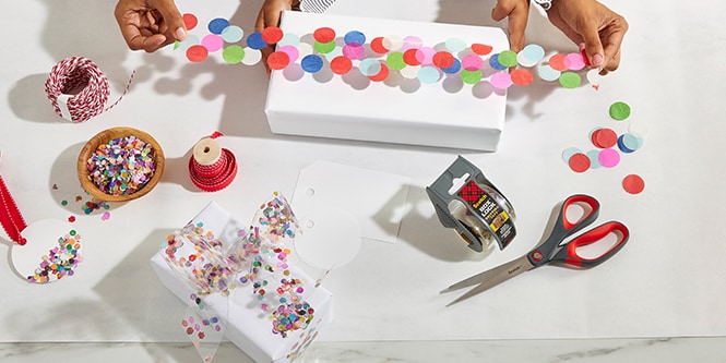 Mujer y su hija envolviendo una caja de regalo con cinta de confeti hecha pegando confeti colorido a la Cinta de Embalaje Scotch®
